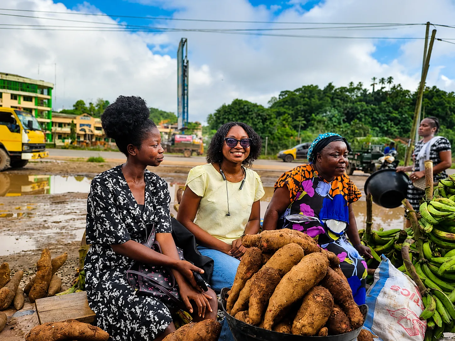 Kuapa Dwaso team members seated beside cassava and plantain while speaking with a trader in Tarkwa